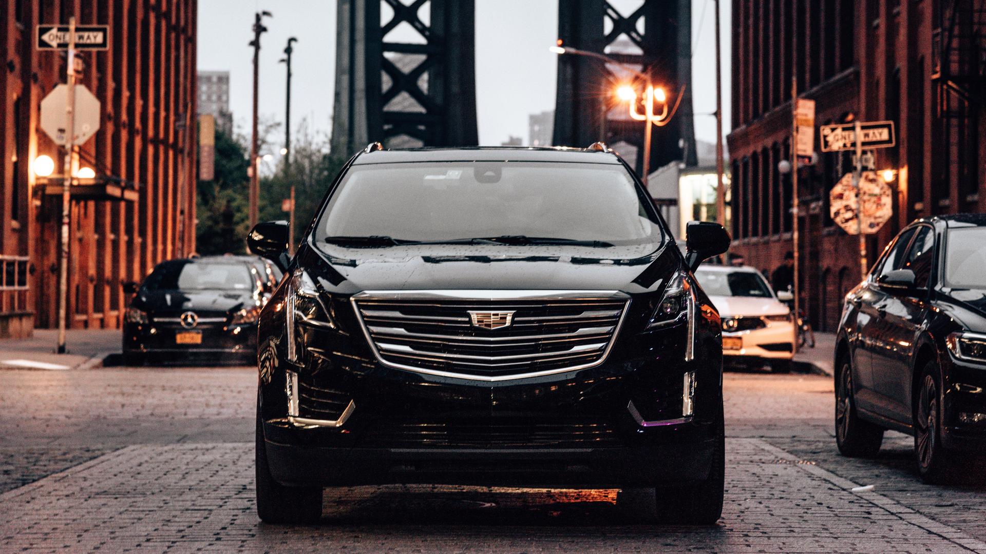 Ein schwarzer SUV im Straßenverkehr in Brooklyn, im Hintergrund ist die Manhattan Bridge zu sehen. 