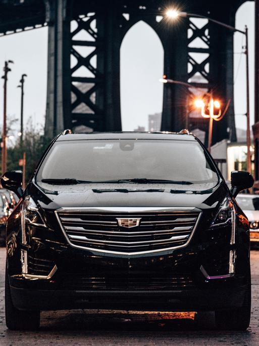 Ein schwarzer SUV im Straßenverkehr in Brooklyn, im Hintergrund ist die Manhattan Bridge zu sehen. 
