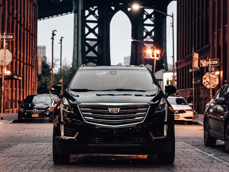 Ein schwarzer SUV im Straßenverkehr in Brooklyn, im Hintergrund ist die Manhattan Bridge zu sehen. 