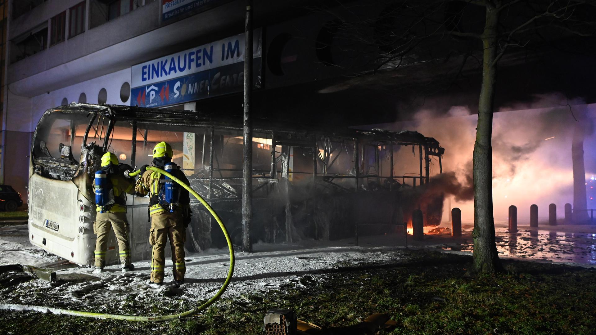 Zwei Feuerwehrmänner löschen an der Sonnenallee in Berlin einen Bus, der von Unbekannten angezündet worden war. 