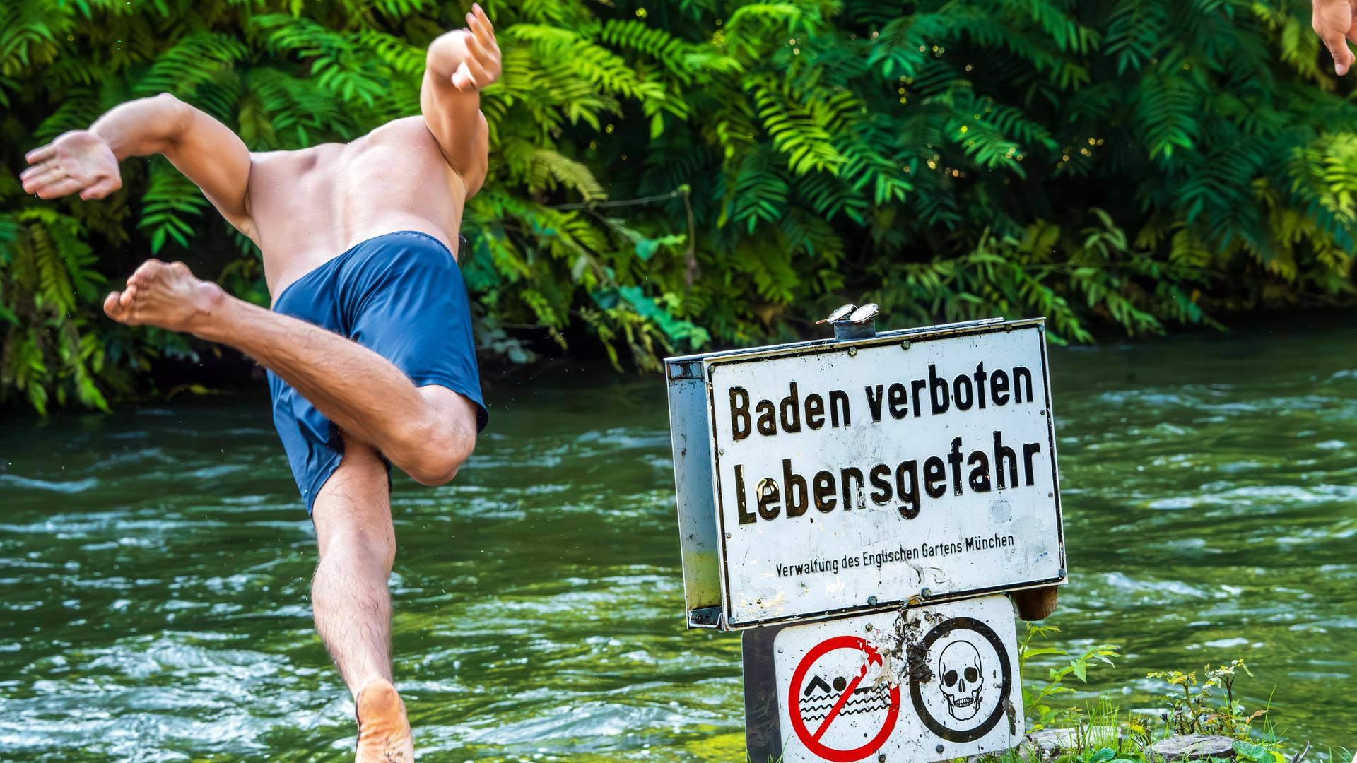 Ein Mann springt trotz Verbotsschild in den Eisbach im Englischen Garten in München. Ein Mann springt trotz Verbotsschild in den Eisbach im Englischen Garten in München.