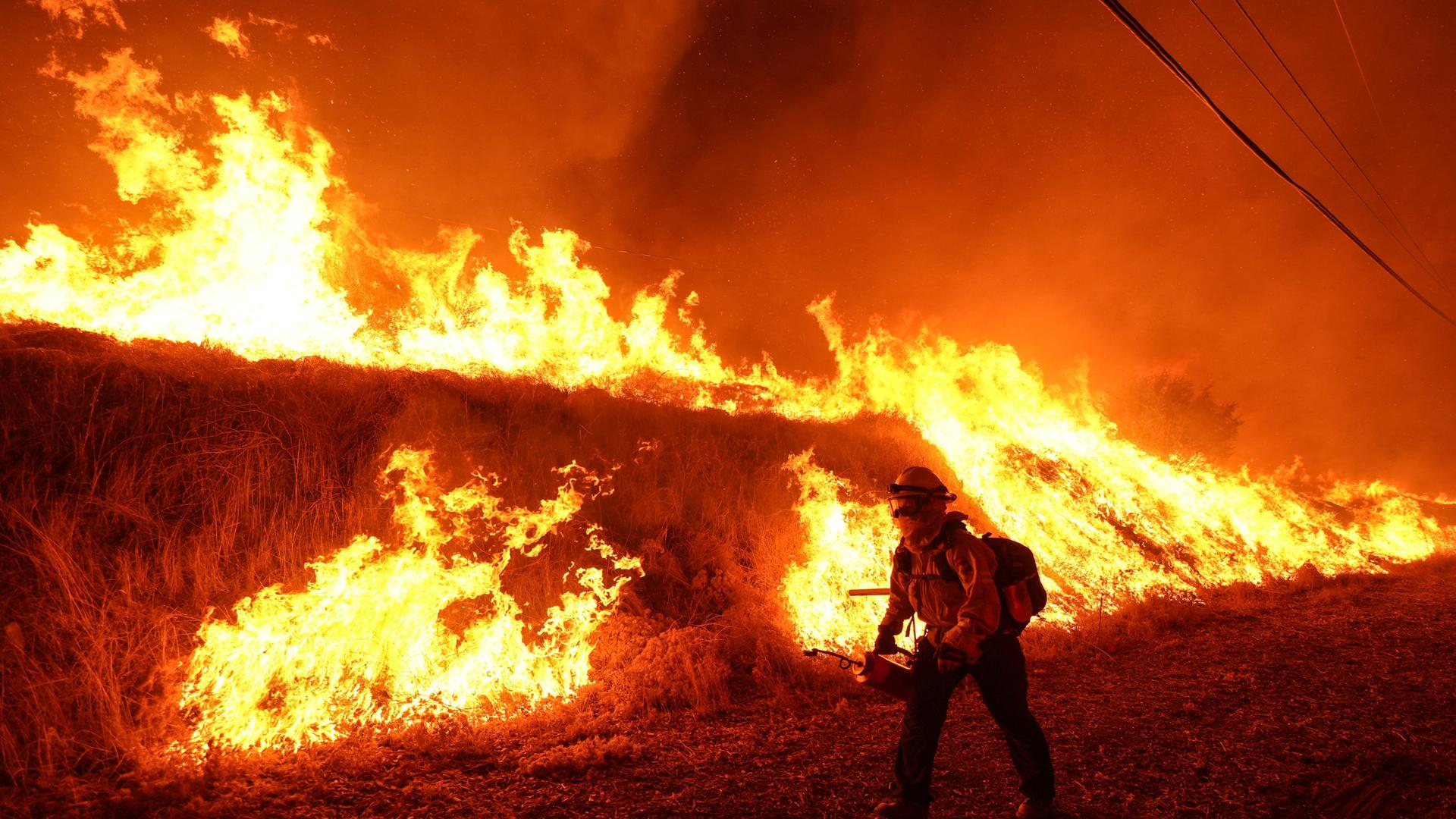 Castaic: Ein Feuerwehrmann trägt eine Flämmkanne, als er ein Gegenfeuer gegen das Hughes-Feuer an einem Berghang entzündet.