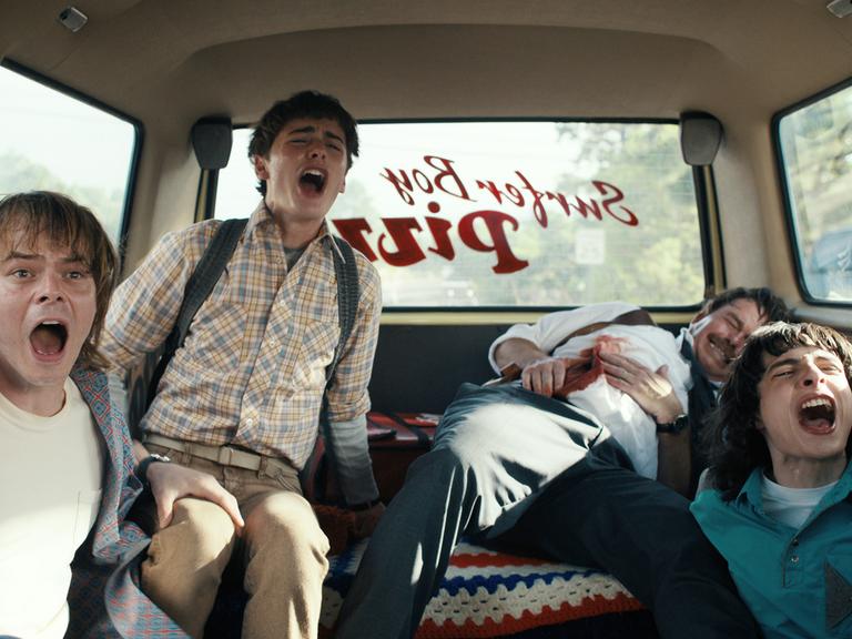 Filmstill: Charlie Heaton als Johnathan Byers, Noah Schnapp als Will Byers and Finn Wolfhard als Mike Wheeler sitzen schreiend im Auto. "Stranger Things" Staffel 4, 2022.