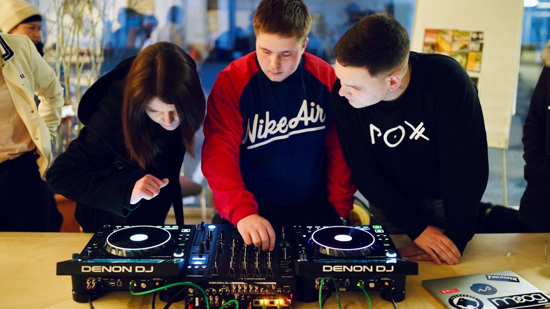 Drei Jugendliche beugen sich über einen Turntable.