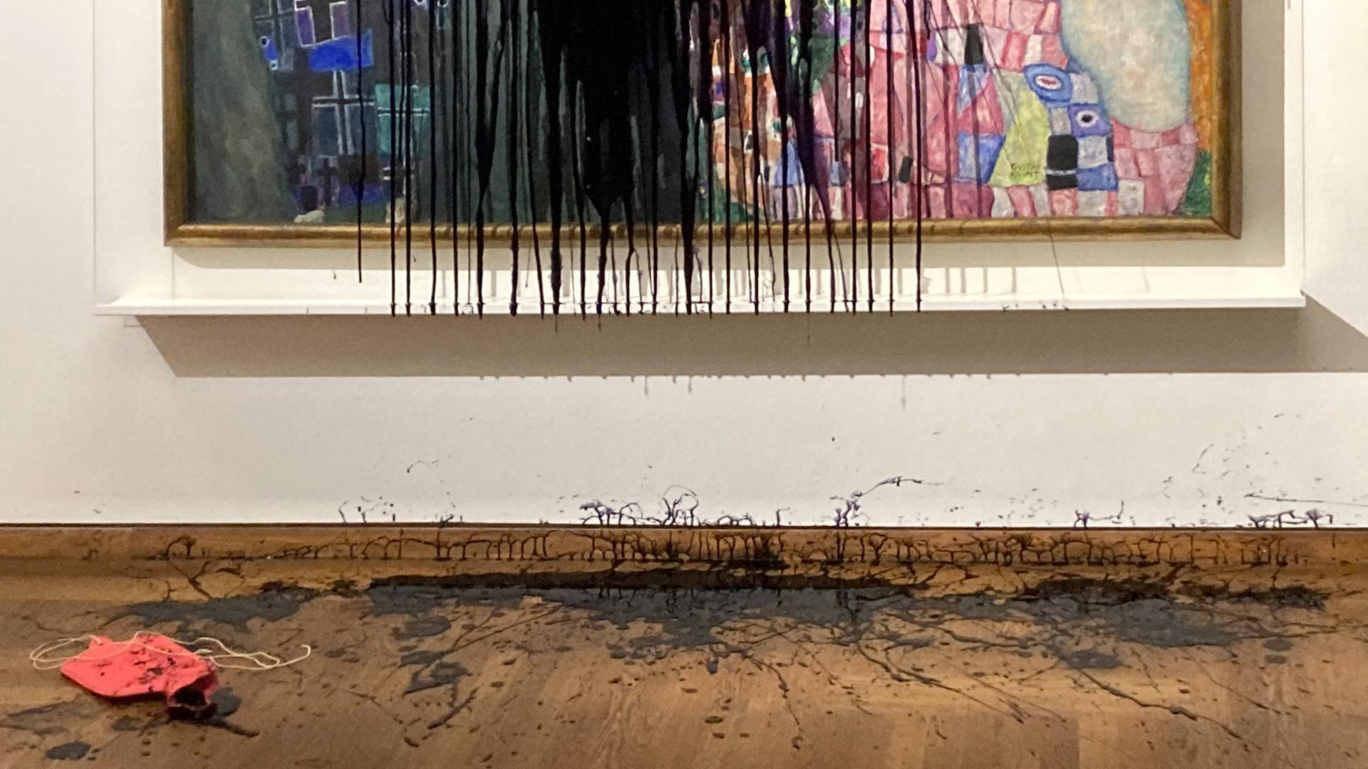 Detail des Gemäldes "Leben und Tod" von Gustav Klimt, was mit schwarzem Öl übergossen ist. Die Wand an der das Gemälde hängt und der Boden des Museums sind ebenfalls mit Öl bedeckt.