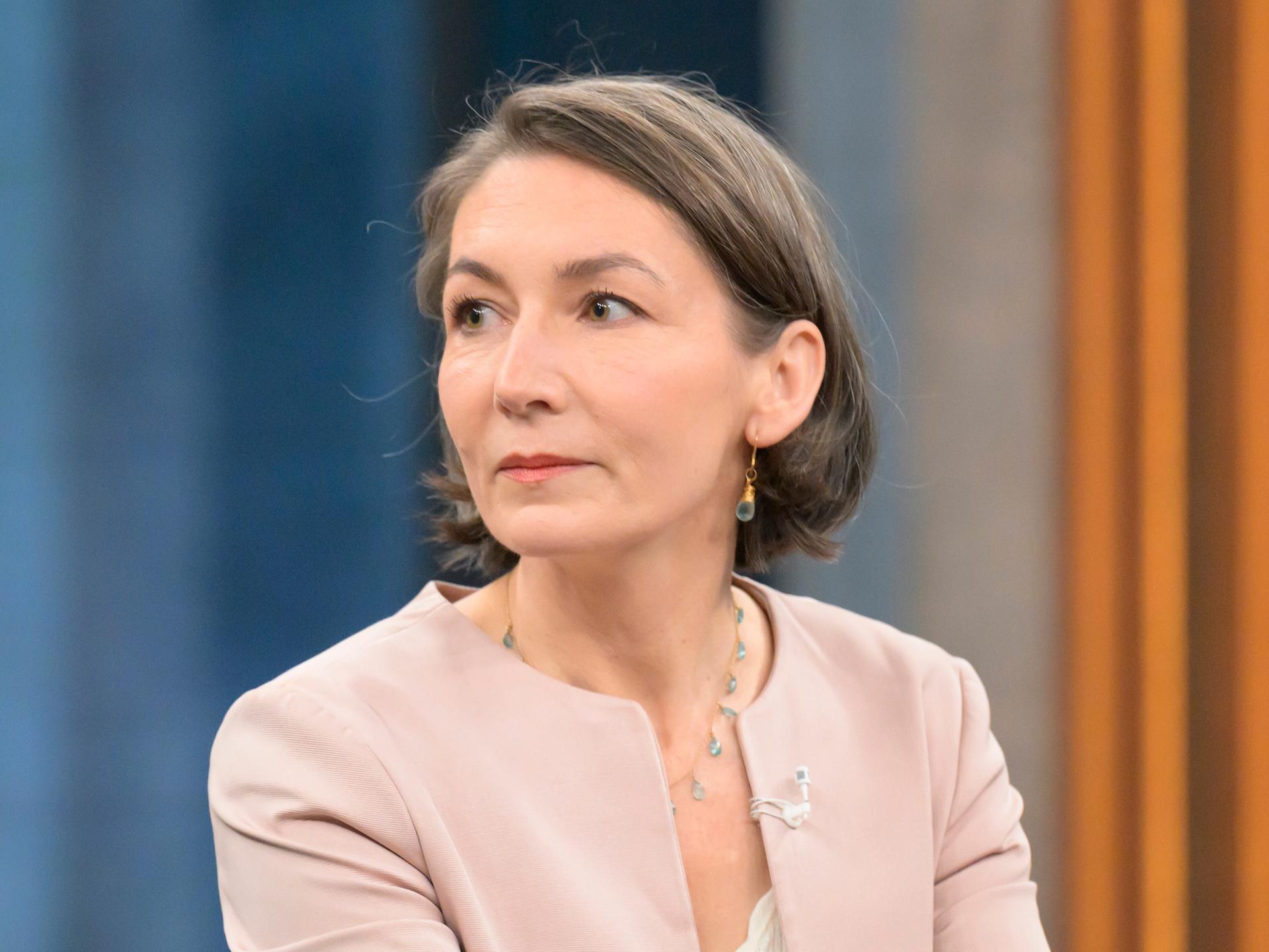 Claudia Major trägt ein helles Sakko und sitzt zur Seite schauend in einem Fernsehstudio mit blaubeigen Hintergrund.