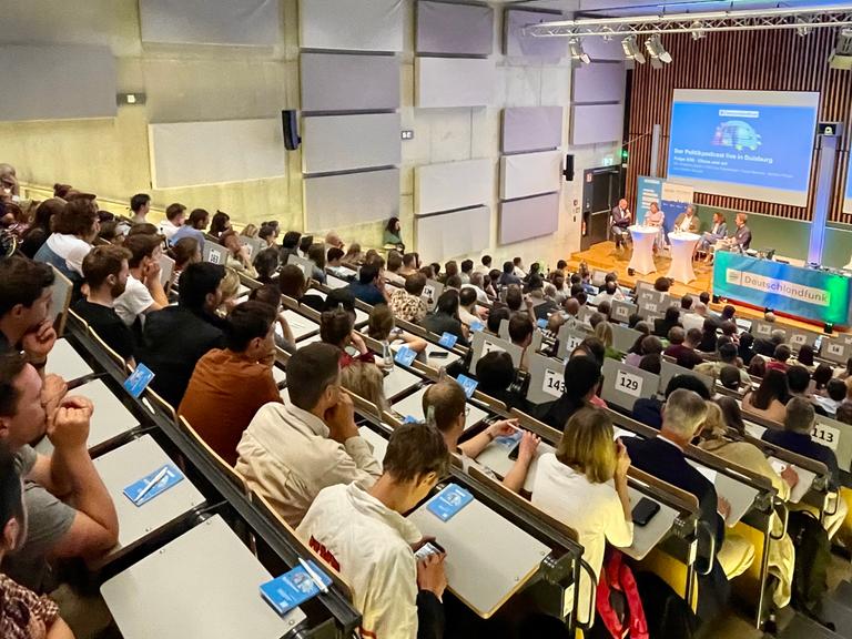 Knapp 200 Menschen lauschen einer Live-Aufzeichnung des Dlf Politkpodcast in einem Hörsaal der Universität Duisburg-Essen