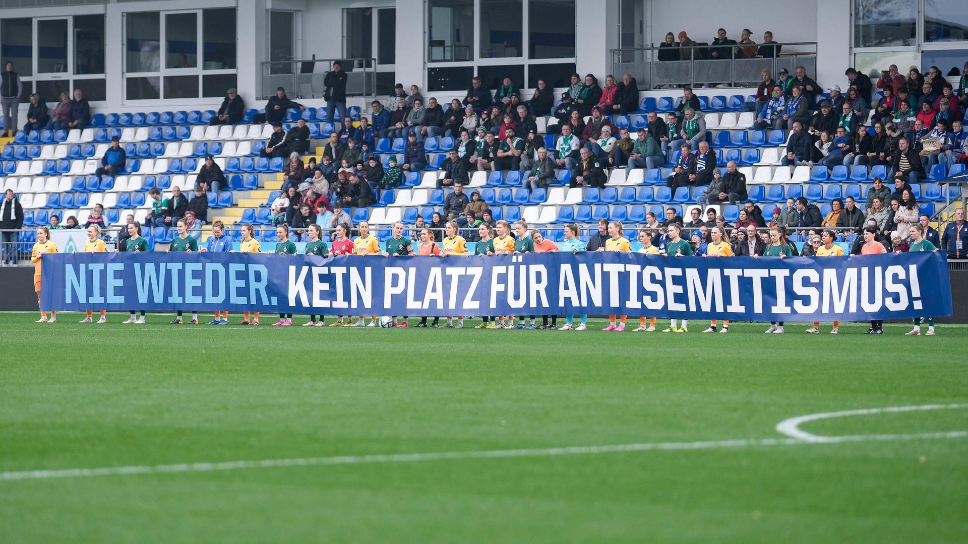 Spielerinnen der TSG 1899 Hoffenheim und Spielerinnen vom SV Werder Bremen mit einem Spruchband mit der Aufschrift: Nie wieder. Kein Platz für Antisemitismus