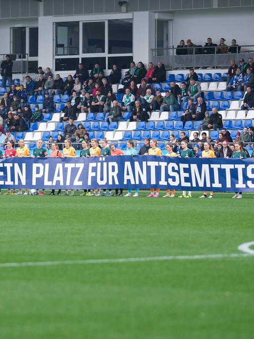 Spielerinnen der TSG 1899 Hoffenheim und Spielerinnen vom SV Werder Bremen mit einem Spruchband mit der Aufschrift: Nie wieder. Kein Platz für Antisemitismus