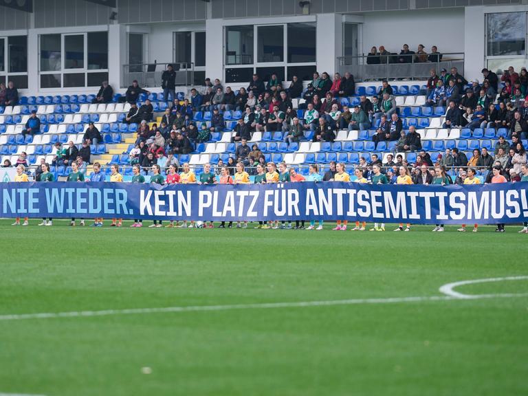 Spielerinnen der TSG 1899 Hoffenheim und Spielerinnen vom SV Werder Bremen mit einem Spruchband mit der Aufschrift: Nie wieder. Kein Platz für Antisemitismus