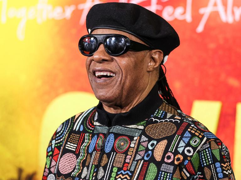 Stevie Wonder lächelt vor einer bunten Wand bei der Premiere des Films "Bob Marley: One Love" in Los Angeles. 