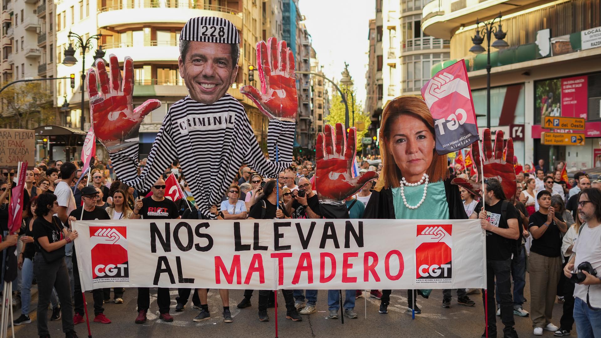 Mehrere Personen tragen auf einer Demonstration zum Jahrestag der Überschwemmungen im spanischen Valencia Spruchbänder und ein Plakat, das den Präsidenten der Region Valencia, Mazón, mit roten Händen zeigt. 
