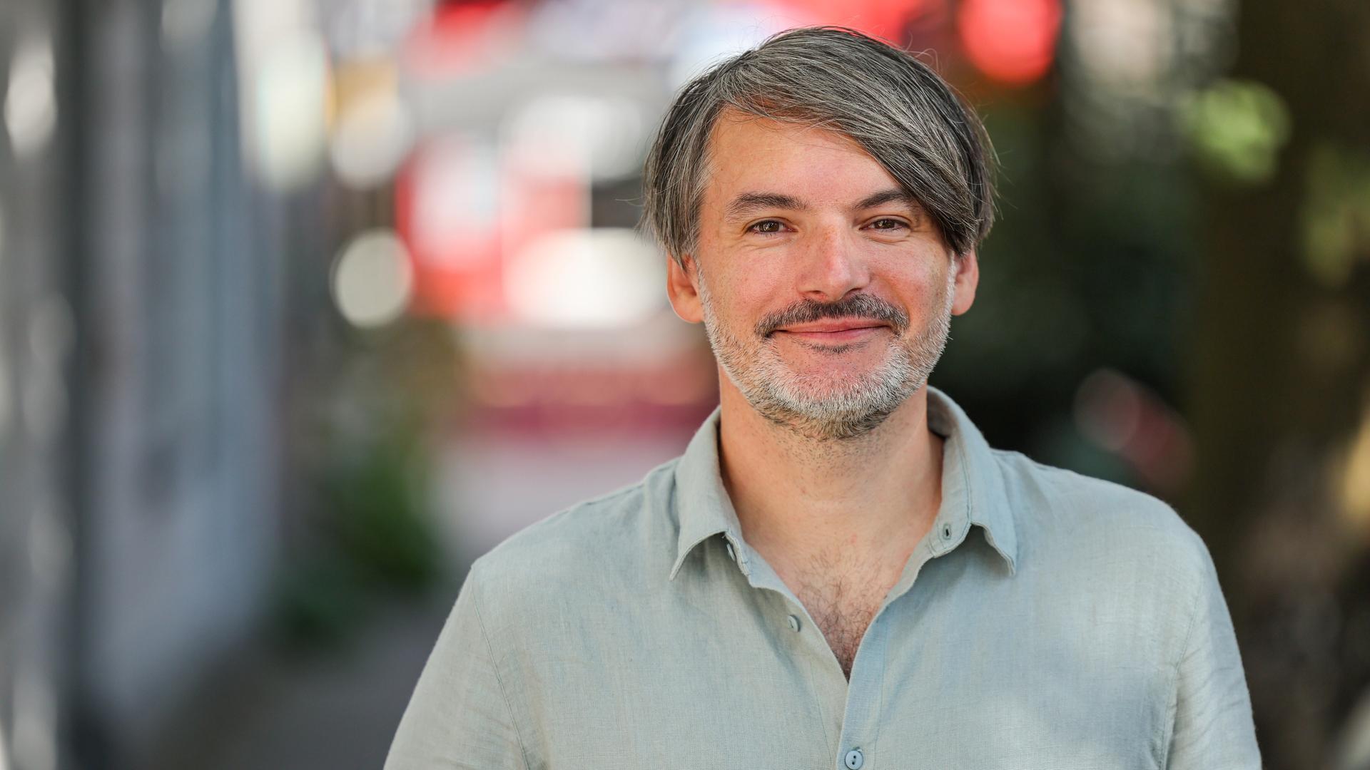 Schriftsteller Saša Stanišić steht auf einer Straße und blickt in die Kamera.