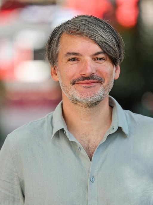 Schriftsteller Saša Stanišić steht auf einer Straße und blickt in die Kamera.