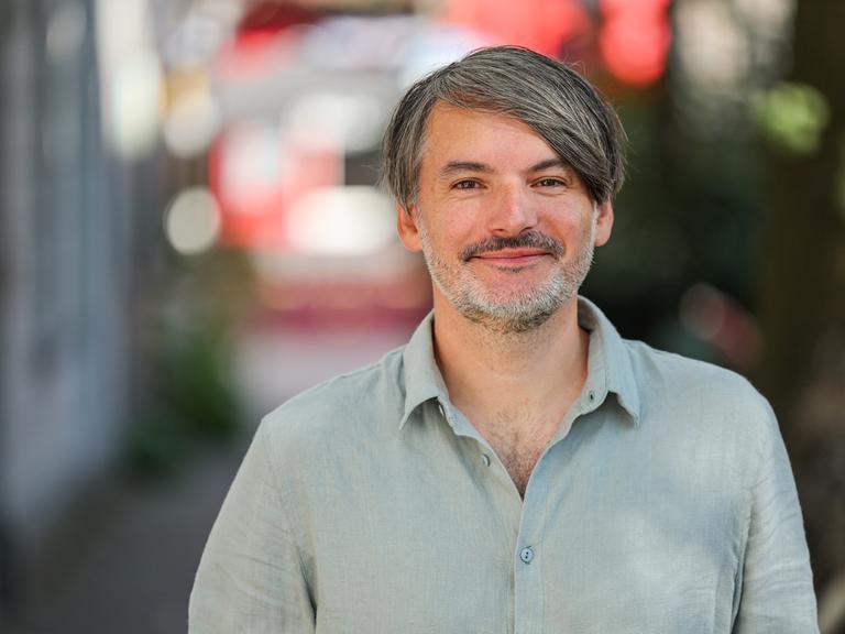 Schriftsteller Saša Stanišić steht auf einer Straße und blickt in die Kamera.