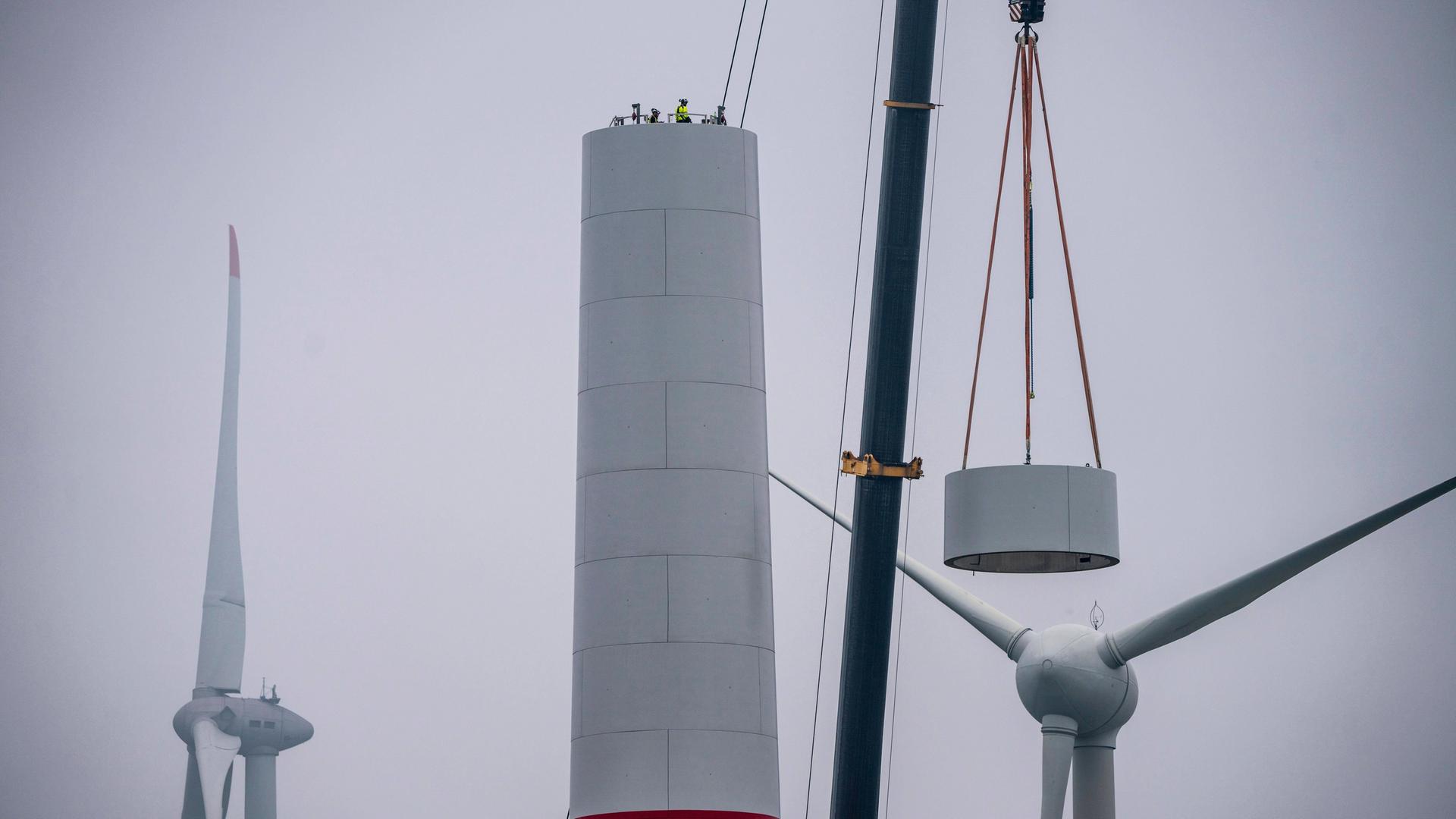 Beim Aufbau des Turm eines Windkraftwerks in einem Windpark bei Issum rieht ein Kran ein Teil eines Windrads in dir Höhe. 
