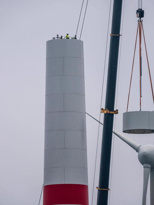 Beim Aufbau des Turm eines Windkraftwerks in einem Windpark bei Issum rieht ein Kran ein Teil eines Windrads in dir Höhe. 