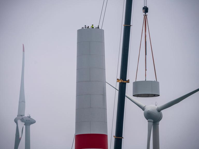 Beim Aufbau des Turm eines Windkraftwerks in einem Windpark bei Issum rieht ein Kran ein Teil eines Windrads in dir Höhe. 