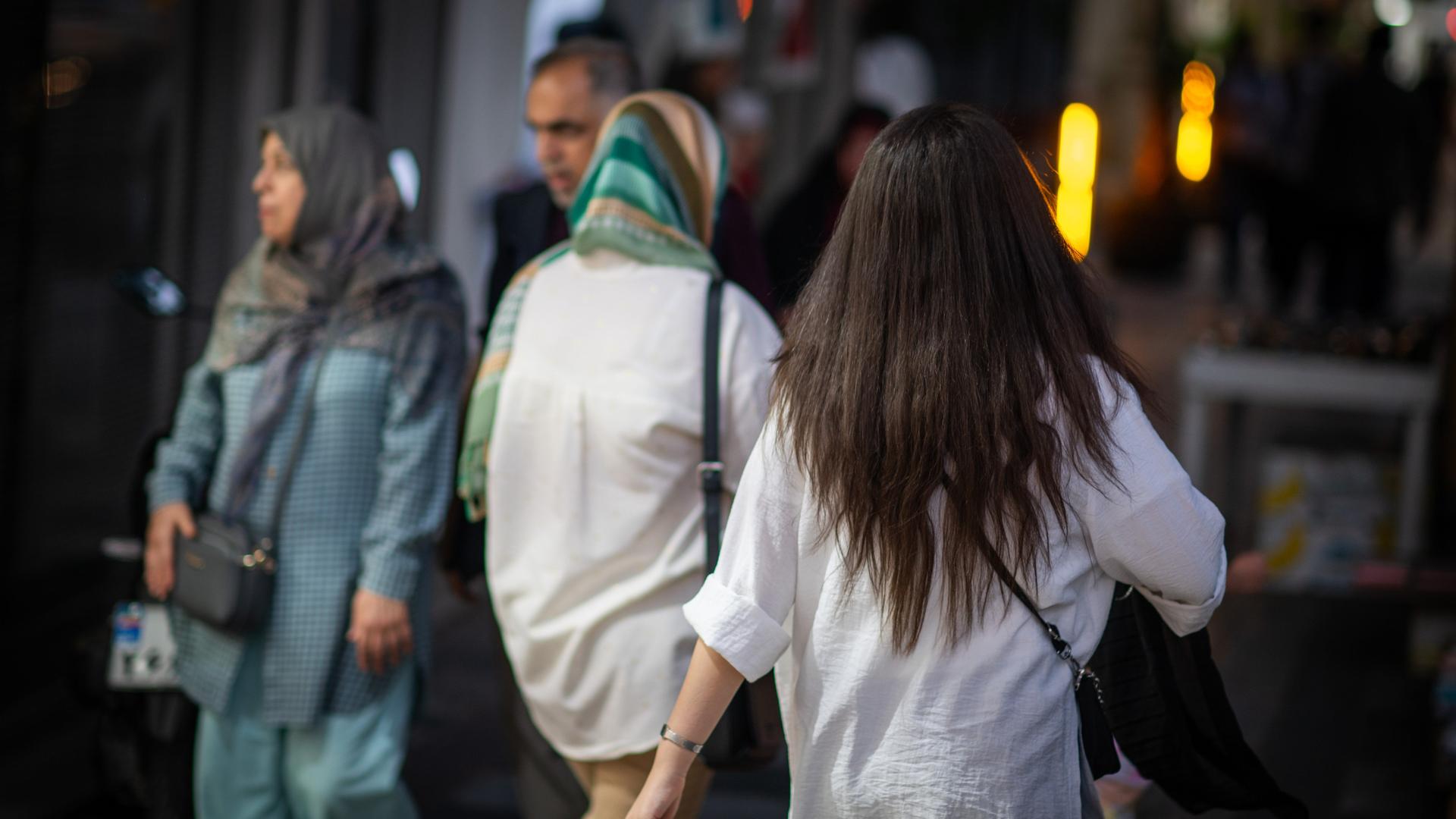 Eine Frau läuft in Teheran mit offenen Haaren am Abend eine Straße entlang.