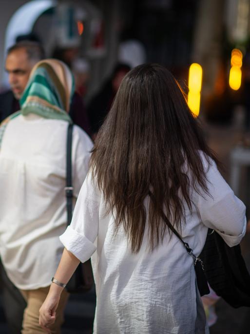 Eine Frau läuft in Teheran mit offenen Haaren am Abend eine Straße entlang. 