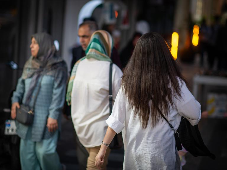 Eine Frau läuft in Teheran mit offenen Haaren am Abend eine Straße entlang. 