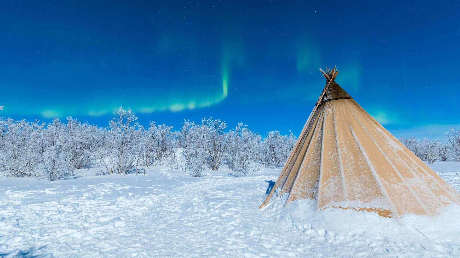 Ein Zelt der indigenen Sami im Schnee mit Nordlichtern am Himmel bei Abisko, Kiruna Municipality, Norrbotten County, Lapland, Schweden.