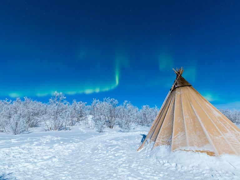 Ein Zelt der indigenen Sami im Schnee mit Nordlichtern am Himmel bei Abisko, Kiruna Municipality, Norrbotten County, Lapland, Schweden.