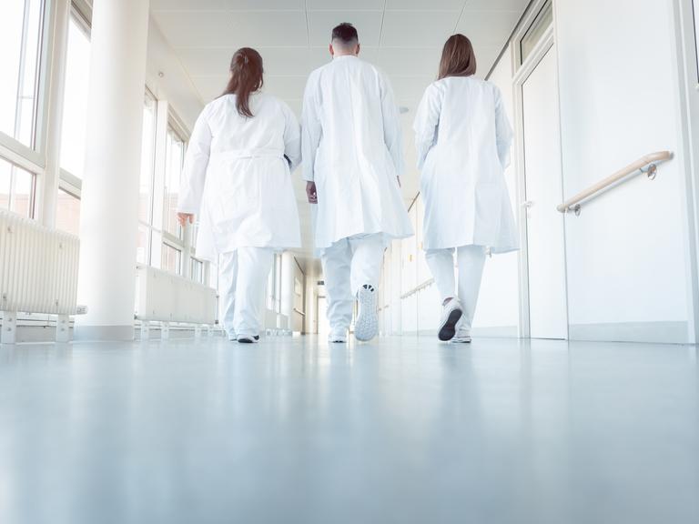 Zwei Ärztinnen und ein Arzt gehen in einem Krankenhausflur.