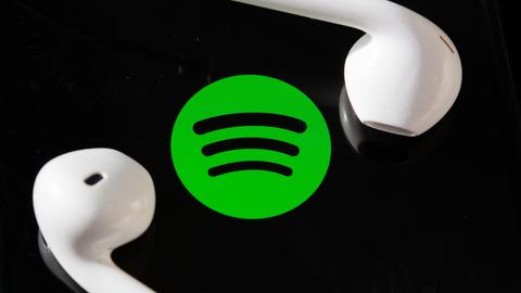 Kopfhörer liegen auf dem Bildschirm eines Smartphones, auf dem das Logo vom Musik-Streaming-Dienst Spotify angezeigt wird.