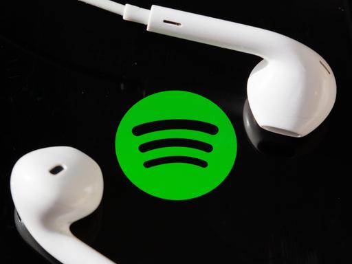 Kopfhörer liegen auf dem Bildschirm eines Smartphones, auf dem das Logo vom Musik-Streaming-Dienst Spotify angezeigt wird.