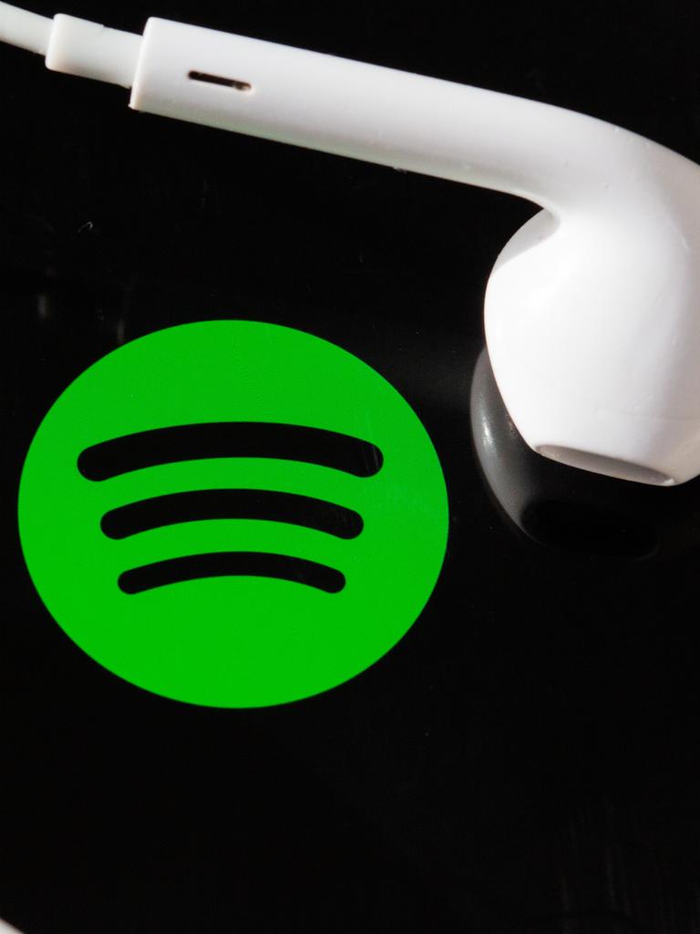 Kopfhörer liegen auf dem Bildschirm eines Smartphones, auf dem das Logo vom Musik-Streaming-Dienst Spotify angezeigt wird.