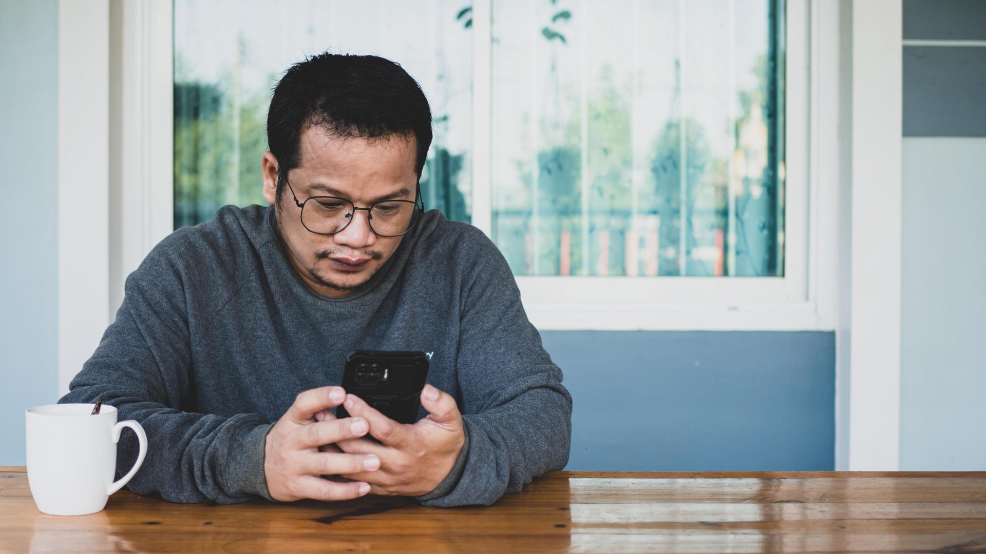 Ein Mann sitzt an einem Tisch und schaut auf ein Smartphone