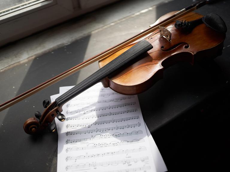 Eine Geige liegt auf einer Fensterbank neben einem Notenpapier.