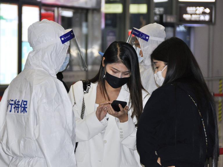 Personen in voller Schutzmontur überprüfen Ankömmlinge an einem Bahnhof in Schanghai auf negative Coronatestbescheinigungen.