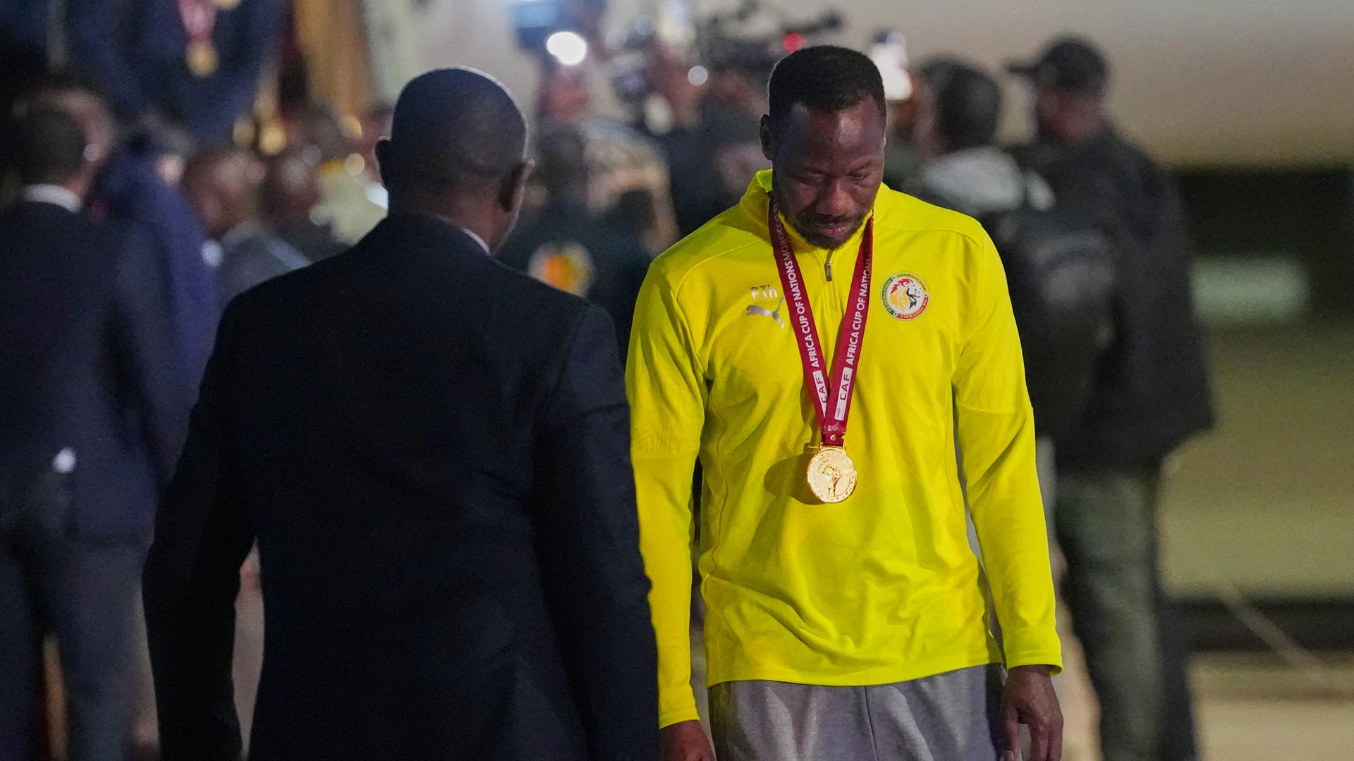 Senegals Trainer Pape Thiaw kommt am Flughafen in Ndiass an, er trägt die Medaille um den Hals.