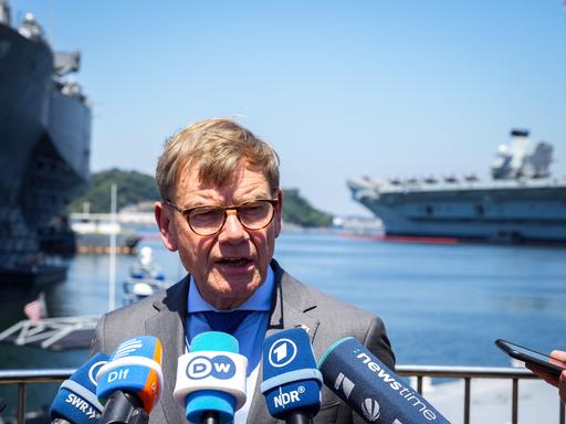 Außenminister Johann Wadephul (CDU) gibt auf dem Stützpunkt der 7. US-Flotte ein Statement. Im Hintergrund stehen das Kommandoschiff USS Blue Ridge (l), rechts das Schiff HMS Prince of Wales der Royal Navy.
