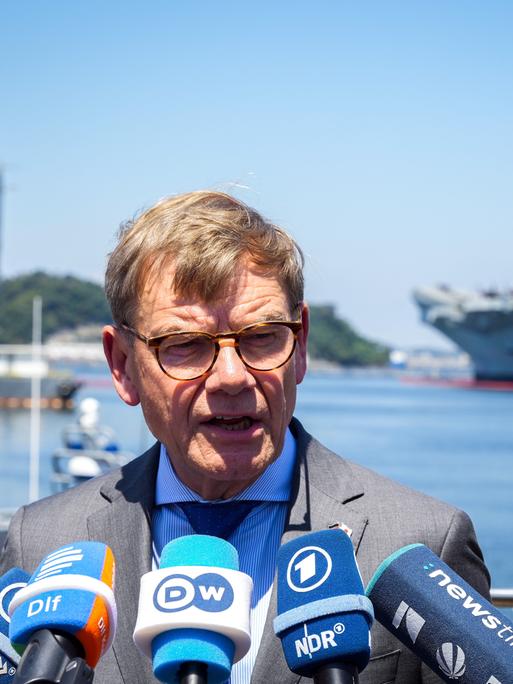 Außenminister Johann Wadephul (CDU) gibt auf dem Stützpunkt der 7. US-Flotte ein Statement. Im Hintergrund stehen das Kommandoschiff USS Blue Ridge (l), rechts das Schiff HMS Prince of Wales der Royal Navy.