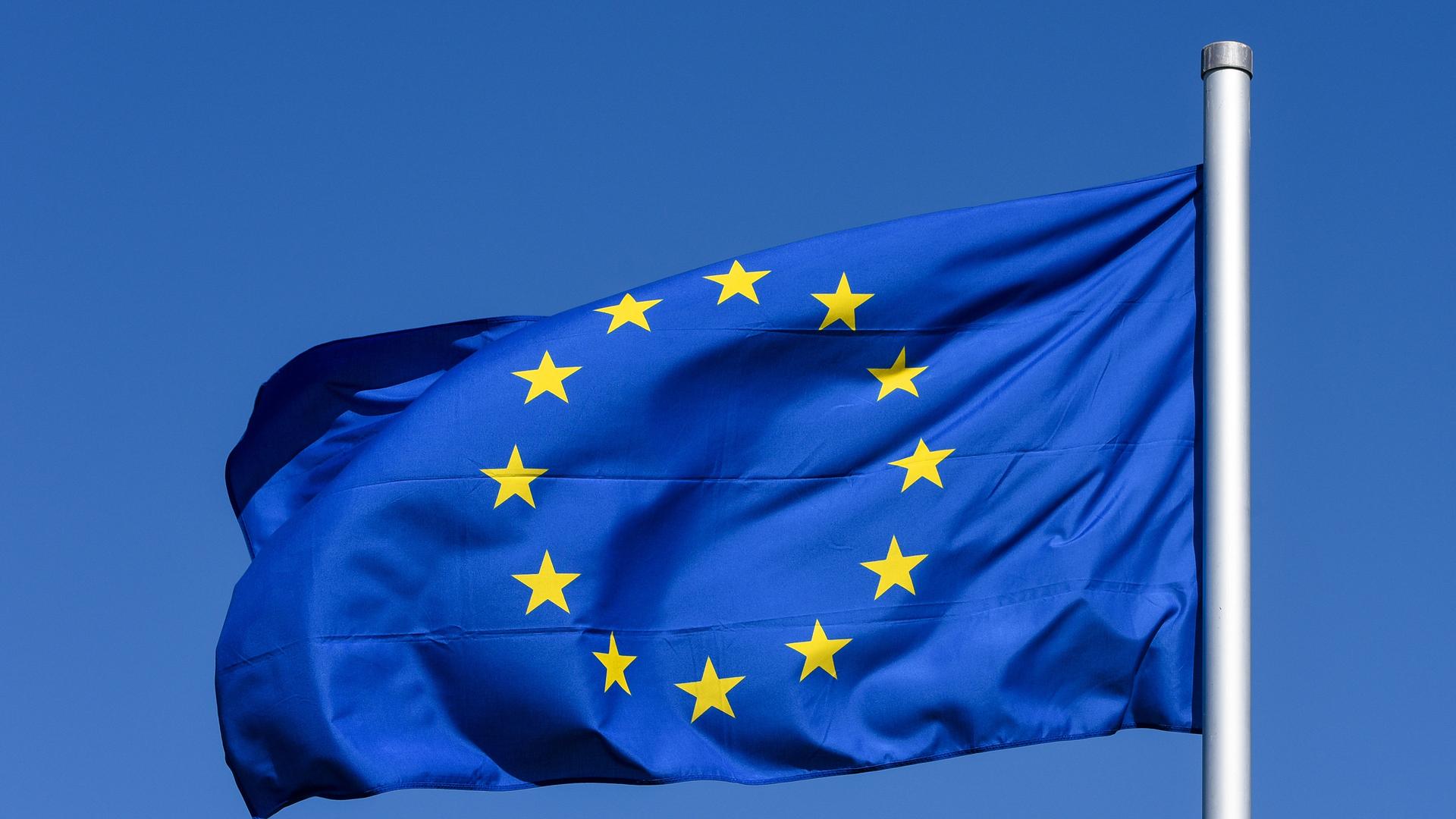 Kiel, eine im Wind wehende Flagge der Europaeischen Union mit den 12 fünfzackigen, gelben Sternen auf azurblauem Hintergrund vor blauem Himmel.