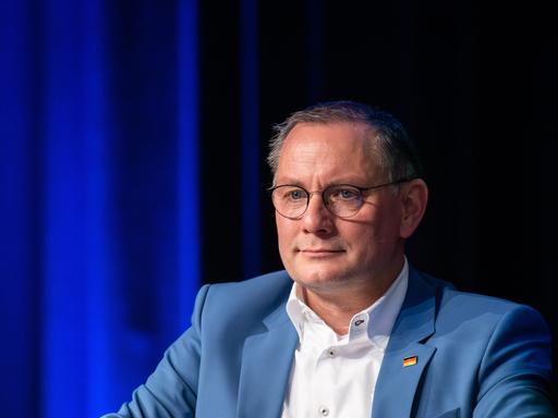 AfD-Bundesvorsitzender Tino Chrupalla in hellblauen Anzug mit weißem Hemd vor blauem Hintergrund.