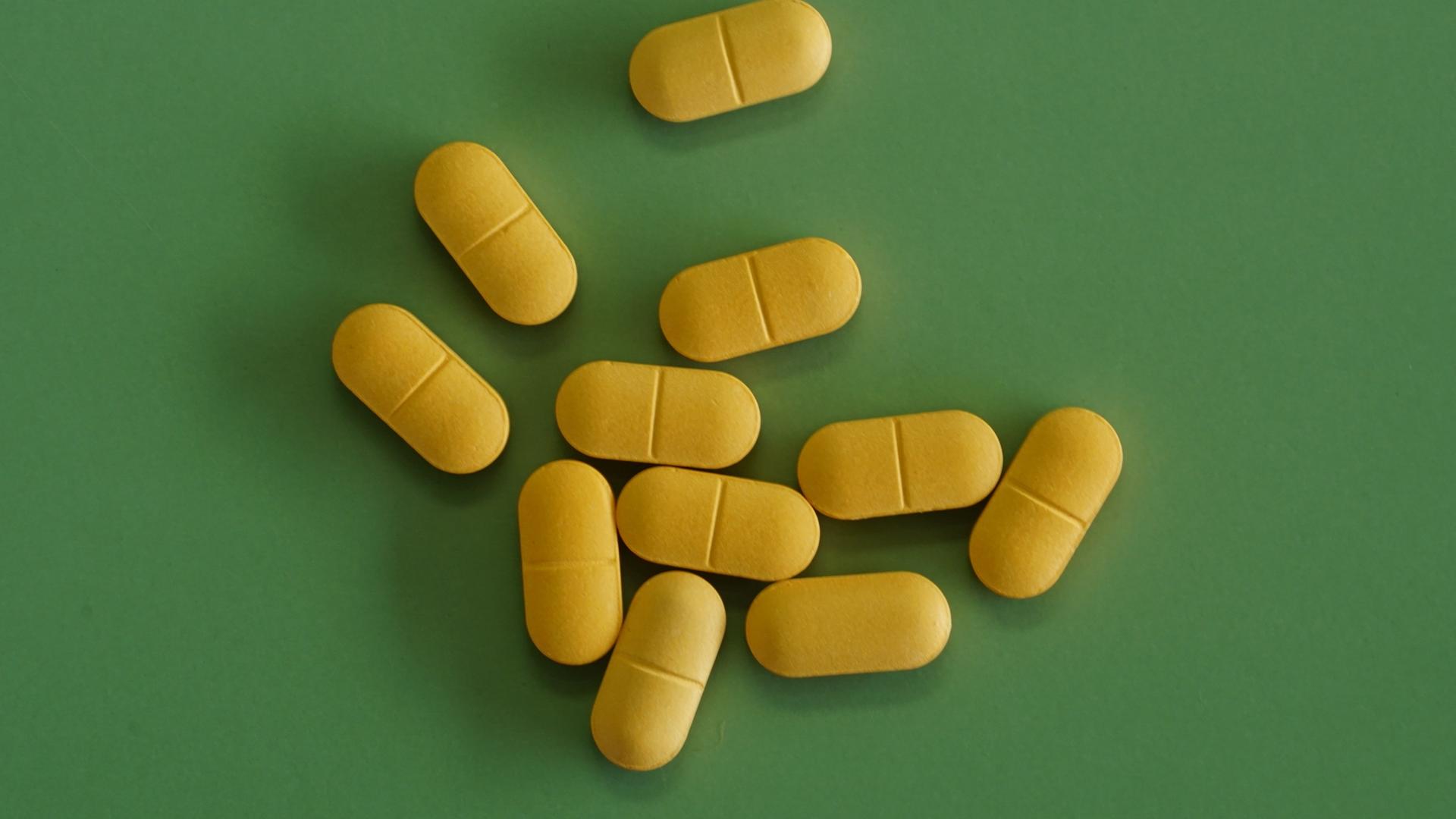 Gelbe, längliche Pillen auf grünem Grund.