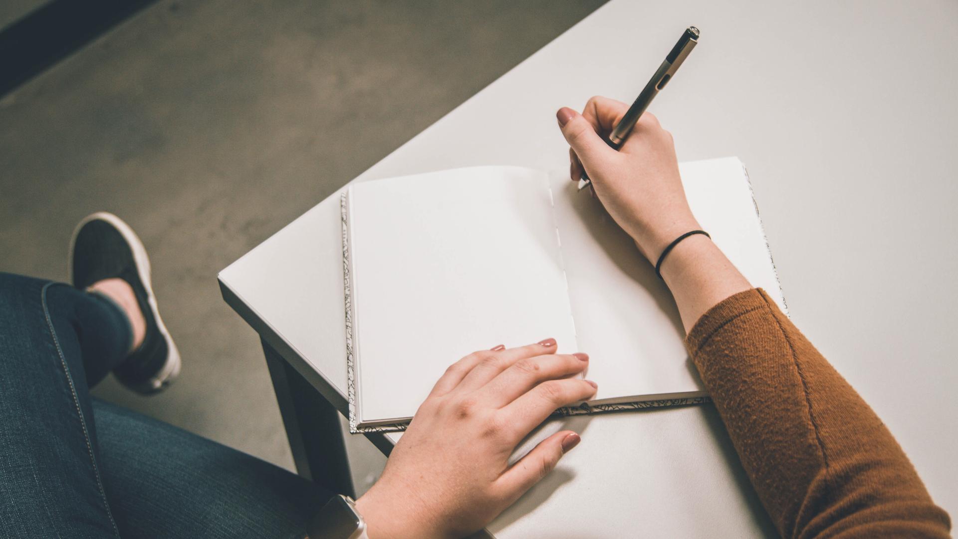 Eine junge Frau sitzt mit einem Stift in der Hand vor einem leeren Blatt Papier. Eine junge Frau sitzt mit einem Stift in der Hand vor einem leeren Blatt Papier.