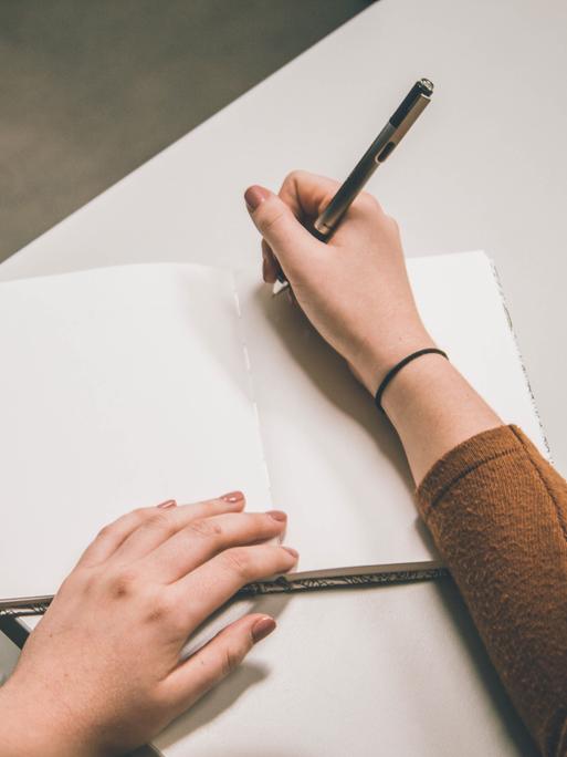 Eine junge Frau sitzt mit einem Stift in der Hand vor einem leeren Blatt Papier.