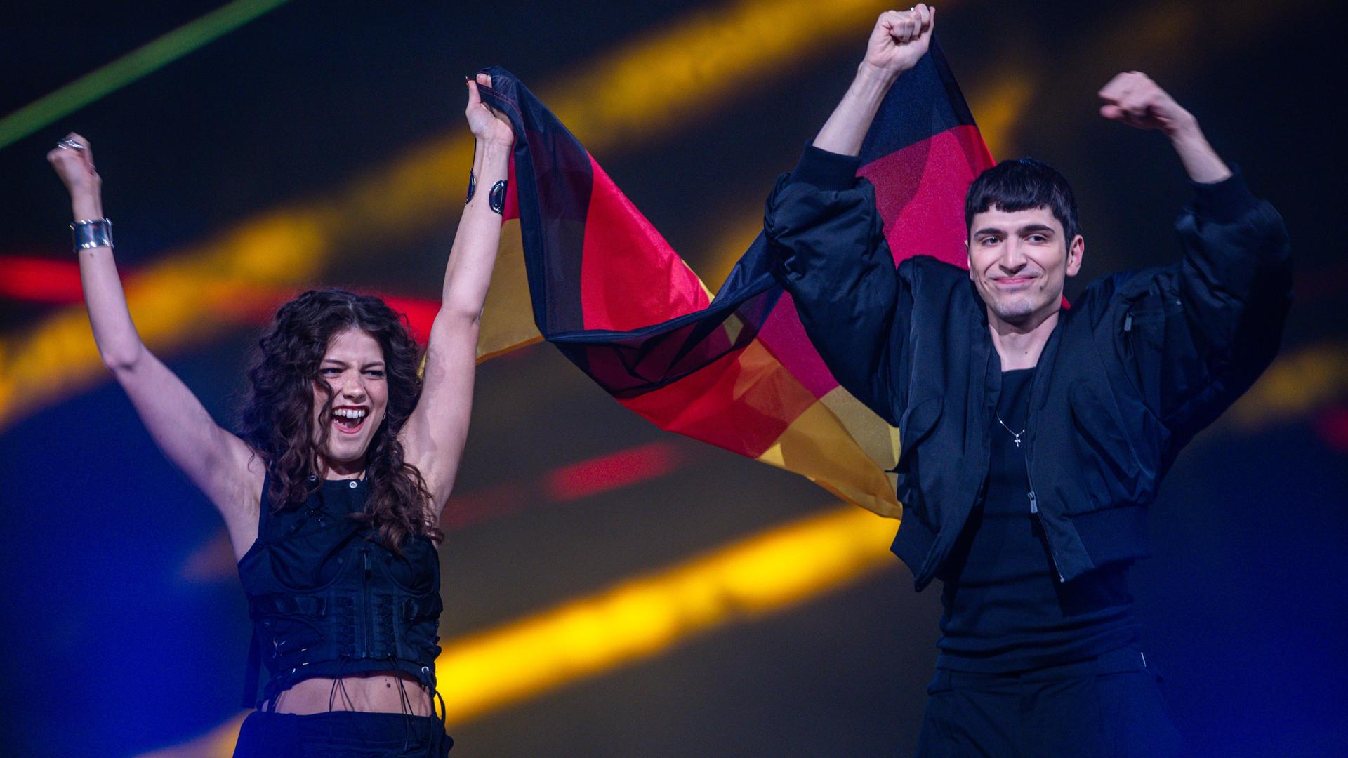 Abor und Tynna stehen auf der Bühne und jubeln. Sie halten eine Deutschland-Fahne. Abor und Tynna stehen auf der Bühne und jubeln. Sie halten eine Deutschland-Fahne.
