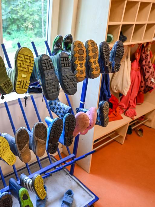 Stiefel und Regenkleidung für Kinder hängen in einer Kita an einem Ständerbeziehungsweise an der Garderobe.
