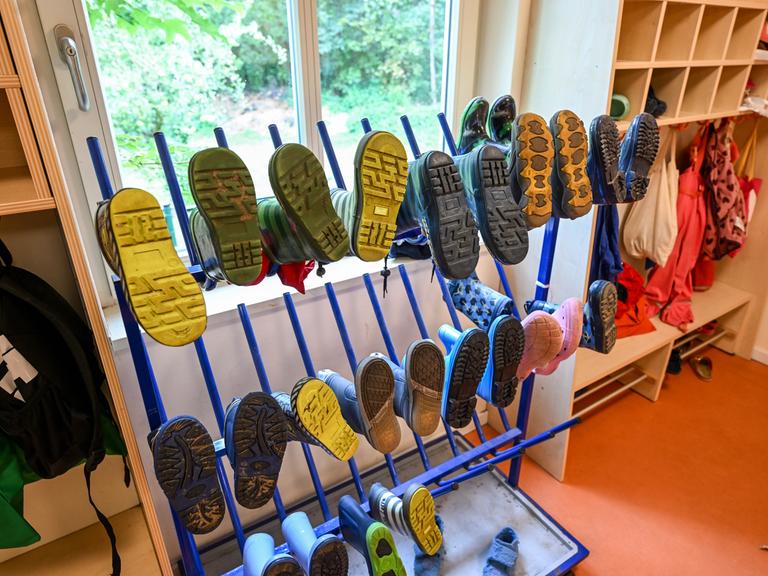 Stiefel und Regenkleidung für Kinder hängen in einer Kita an einem Ständerbeziehungsweise an der Garderobe.
