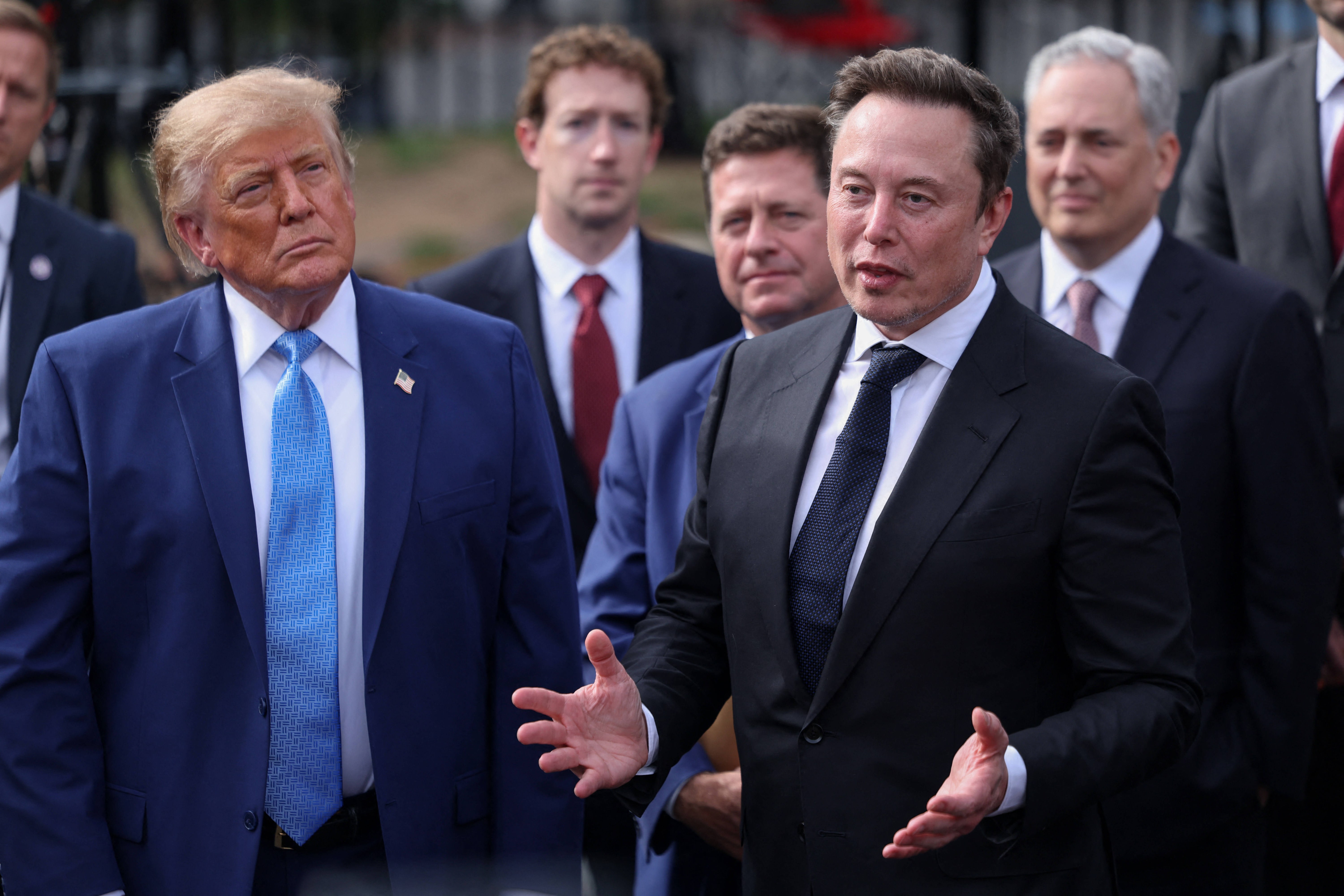 US-Präsident Donald Trump steht links neben Elon Musk, im Hintergrund sind weitere CEOs zu sehen, wie Meta-Chef Mark Zuckerberg