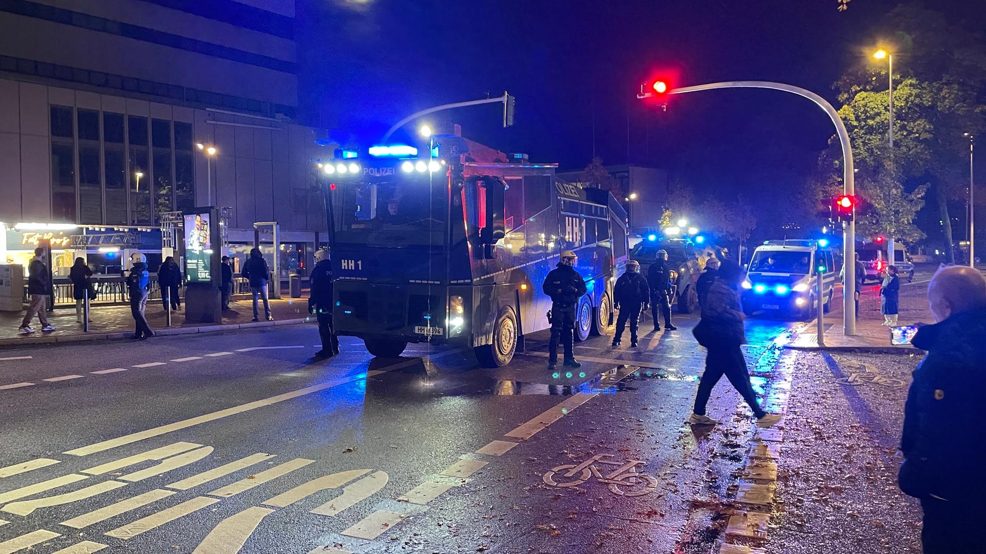 Einsatzkräfte der Polizei stehen neben Einsatzfahrzeugen in Hamburg Harburg. Es ist dunkel draußen und die rote Ampel der Straße und die Signallichter der Einsatzfahrzeuge leuchten grell.