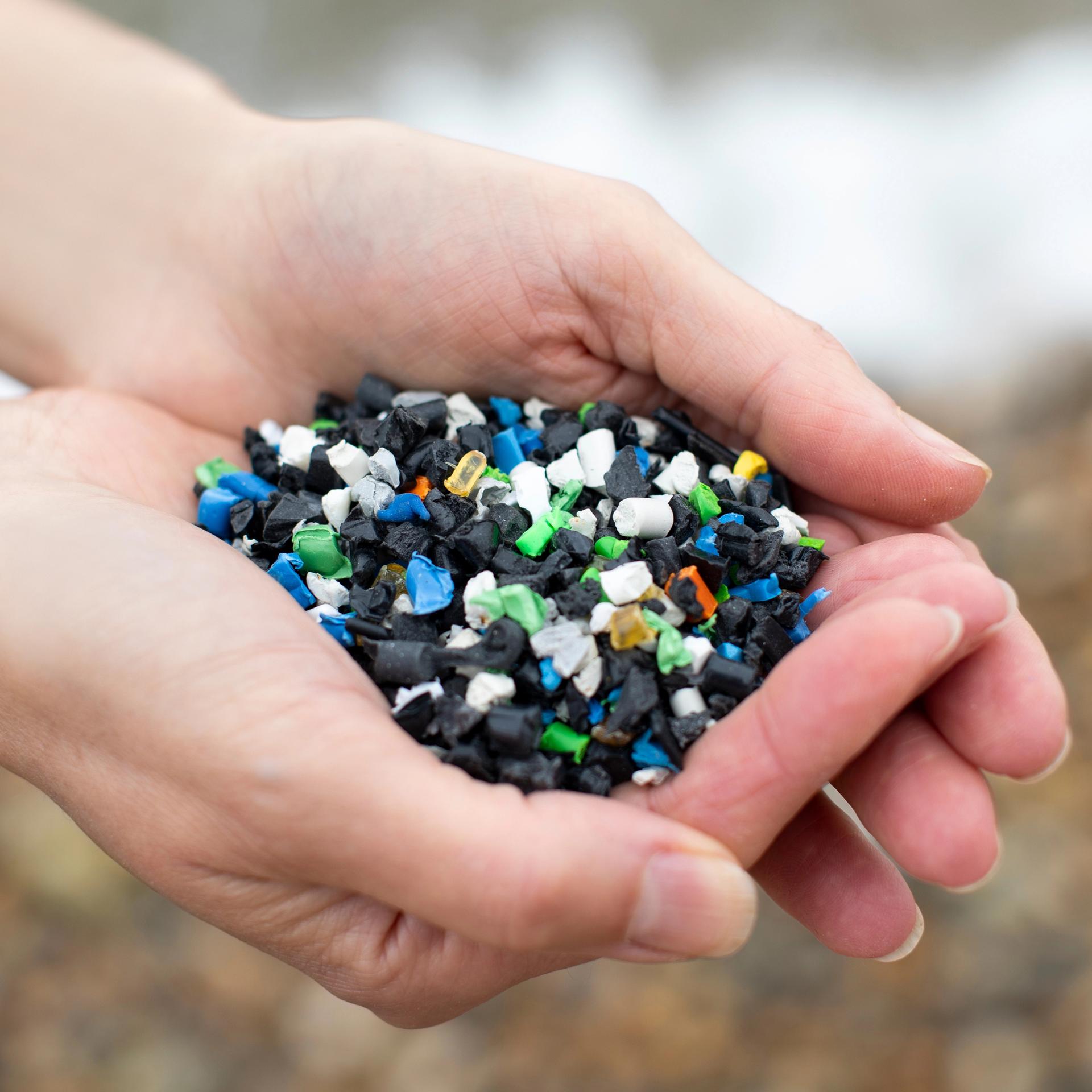Nahaufnahme zweier Hände, die buntes Plastikgranulat halten