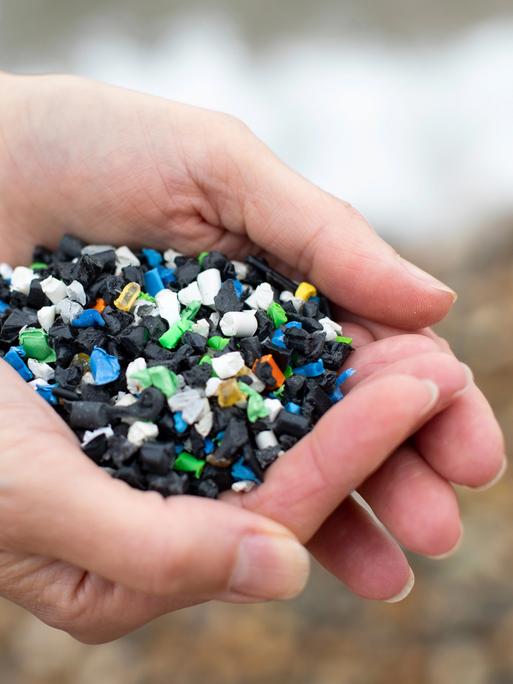 Nahaufnahme zweier Hände, die buntes Plastikgranulat halten