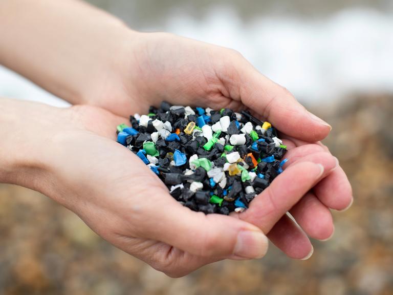 Nahaufnahme zweier Hände, die buntes Plastikgranulat halten